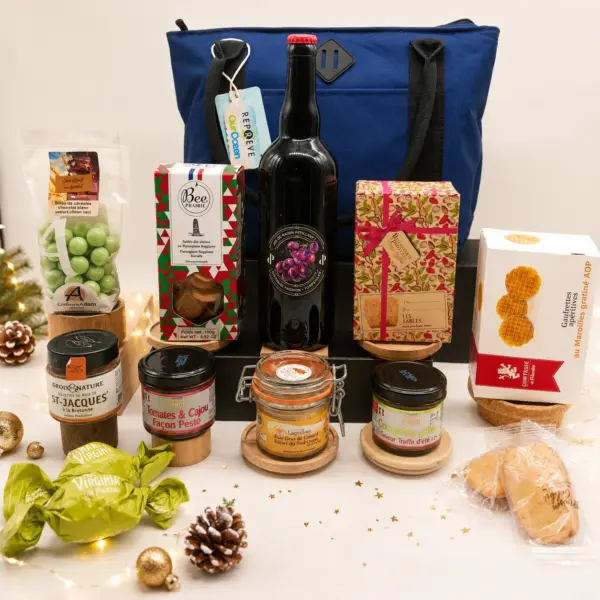 Coffret gourmand de Noël présenté devant un sac bleu, avec bouteille, biscuits, tartinables, gaufrettes et douceurs sucrées.